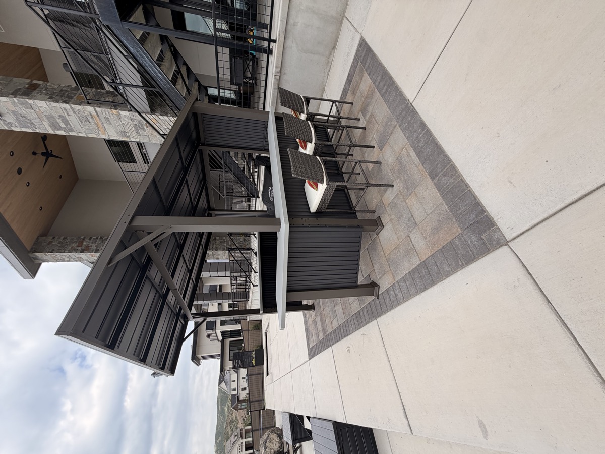 An outdoor kitchen under a louvered pergola on a grey paver patio