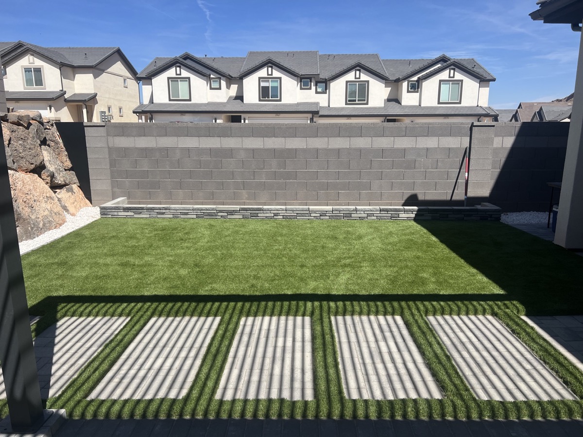 A backyard with artificial turf above a block retaining wall